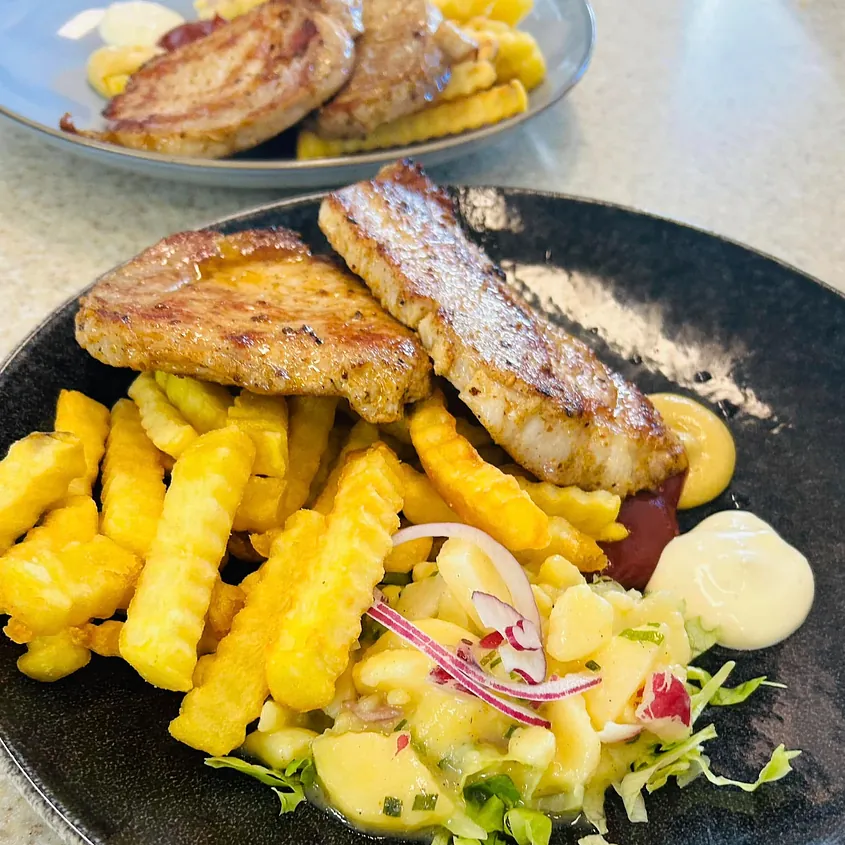 Zart gegrilltes Schweinekotelett mit Pommes frites, Kartoffelsalat mit Zwiebeln und cremigen Saucen